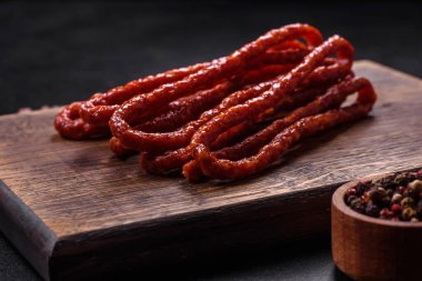 Lezzetli ince tütsülenmiş et sosisleri, baharatlar ve otlar koyu beton arka planda.