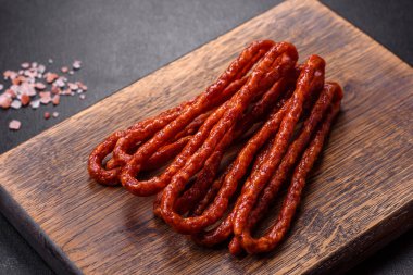 Lezzetli ince tütsülenmiş et sosisleri, baharatlar ve otlar koyu beton arka planda.