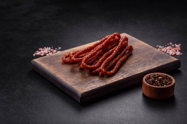 Lezzetli ince tütsülenmiş et sosisleri, baharatlar ve otlar koyu beton arka planda.