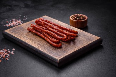 Lezzetli ince tütsülenmiş et sosisleri, baharatlar ve otlar koyu beton arka planda.