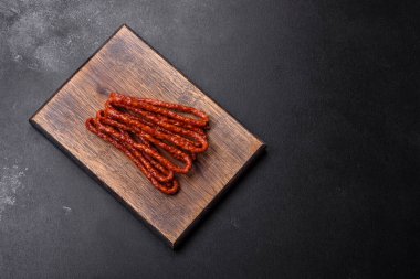 Lezzetli ince tütsülenmiş et sosisleri, baharatlar ve otlar koyu beton arka planda.