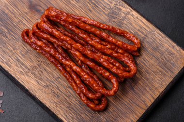 Lezzetli ince tütsülenmiş et sosisleri, baharatlar ve otlar koyu beton arka planda.