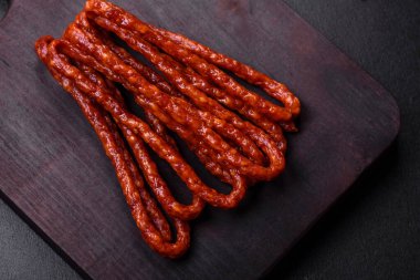 Lezzetli ince tütsülenmiş et sosisleri, baharatlar ve otlar koyu beton arka planda.