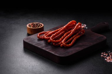 Lezzetli ince tütsülenmiş et sosisleri, baharatlar ve otlar koyu beton arka planda.