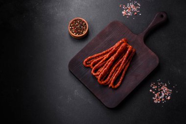 Lezzetli ince tütsülenmiş et sosisleri, baharatlar ve otlar koyu beton arka planda.