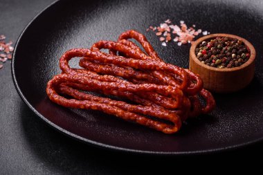 Lezzetli ince tütsülenmiş et sosisleri, baharatlar ve otlar koyu beton arka planda.