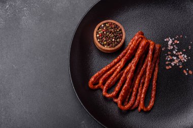 Lezzetli ince tütsülenmiş et sosisleri, baharatlar ve otlar koyu beton arka planda.