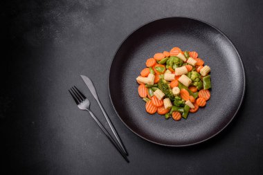 Sebze karışımı: havuç, küçük mısır başları, siyah seramik tabakta pişirilmiş kuşkonmaz fasulyeleri.