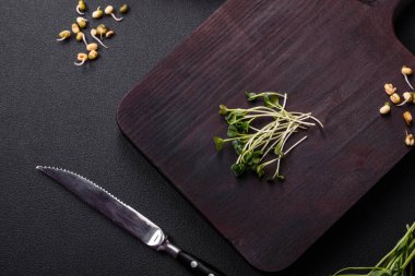 Porsiyonlu plastik bir kutunun içinde koyu beton bir arka planda bezelye, hardal ve filizlenmiş mung fasulyesi mikro yeşillikleri.