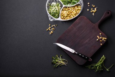 Porsiyonlu plastik bir kutunun içinde koyu beton bir arka planda bezelye, hardal ve filizlenmiş mung fasulyesi mikro yeşillikleri.