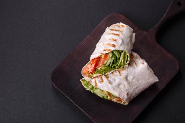 Lezzetli taze shawarma domates, biber, salatalık ve soslu koyu beton arka planda. Fast food