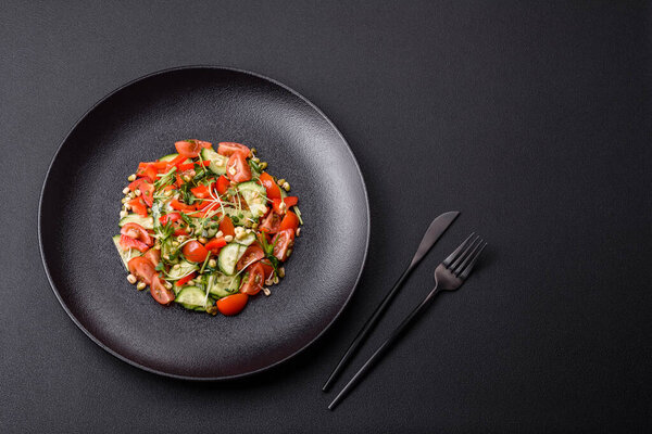 Delicious juicy fresh salad of tomatoes, peppers, cucumber, microgreens and sprouted  mung bean on a black ceramic plate on a dark concrete background