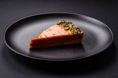 Beautiful tasty pumpkin pie with slices on a black ceramic plate on a dark concrete background