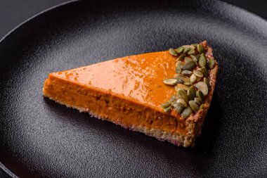 Beautiful tasty pumpkin pie with slices on a black ceramic plate on a dark concrete background