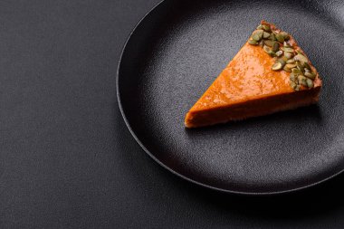 Beautiful tasty pumpkin pie with slices on a black ceramic plate on a dark concrete background