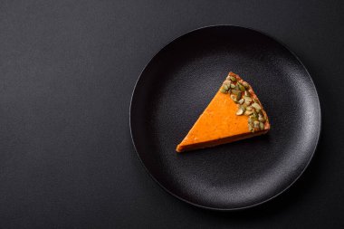 Beautiful tasty pumpkin pie with slices on a black ceramic plate on a dark concrete background