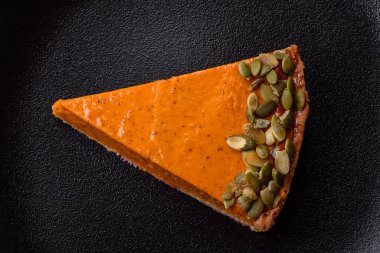 Beautiful tasty pumpkin pie with slices on a black ceramic plate on a dark concrete background