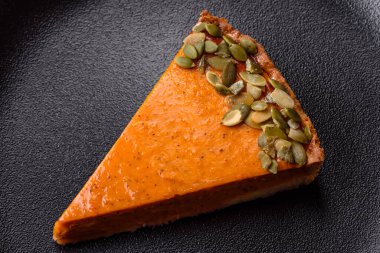 Beautiful tasty pumpkin pie with slices on a black ceramic plate on a dark concrete background