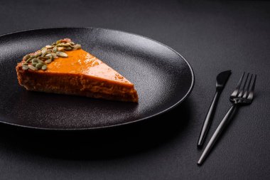 Beautiful tasty pumpkin pie with slices on a black ceramic plate on a dark concrete background