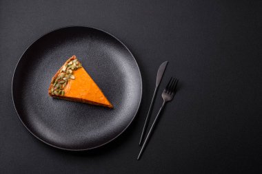 Beautiful tasty pumpkin pie with slices on a black ceramic plate on a dark concrete background