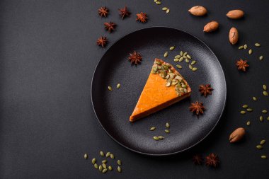 Beautiful tasty pumpkin pie with slices on a black ceramic plate on a dark concrete background