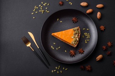 Beautiful tasty pumpkin pie with slices on a black ceramic plate on a dark concrete background