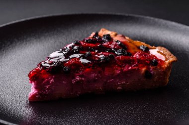 Delicious fresh pie with raspberries and other berries and cheese on a dark plate on a black background