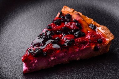 Delicious fresh pie with raspberries and other berries and cheese on a dark plate on a black background