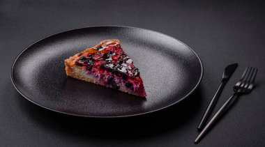 Delicious fresh pie with raspberries and other berries and cheese on a dark plate on a black background