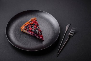 Delicious fresh pie with raspberries and other berries and cheese on a dark plate on a black background