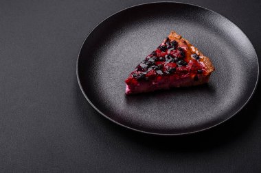 Delicious fresh pie with raspberries and other berries and cheese on a dark plate on a black background