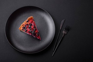 Delicious fresh pie with raspberries and other berries and cheese on a dark plate on a black background
