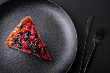 Delicious fresh pie with raspberries and other berries and cheese on a dark plate on a black background