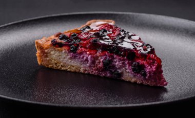 Delicious fresh pie with raspberries and other berries and cheese on a dark plate on a black background
