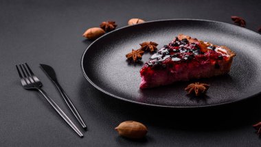 Delicious fresh pie with raspberries and other berries and cheese on a dark plate on a black background