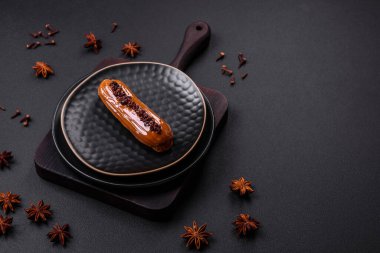 Delicious fresh eclair with chocolate cream on a black ceramic plate on a dark concrete background