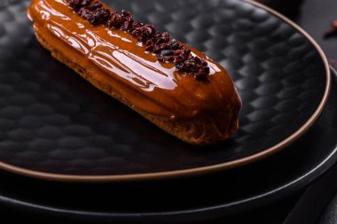 Delicious fresh eclair with chocolate cream on a black ceramic plate on a dark concrete background