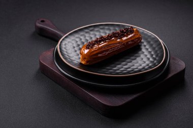 Delicious fresh eclair with chocolate cream on a black ceramic plate on a dark concrete background