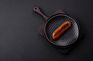 Delicious fresh eclair with chocolate cream on a black ceramic plate on a dark concrete background