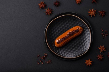 Delicious fresh eclair with chocolate cream on a black ceramic plate on a dark concrete background