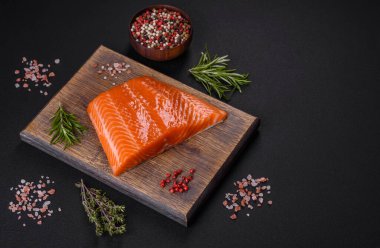 Fillet of raw red salmon fish with salt, spices and herbs on a dark concrete background