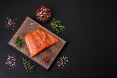 Fillet of raw red salmon fish with salt, spices and herbs on a dark concrete background
