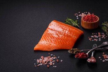 Fillet of raw red salmon fish with salt, spices and herbs on a dark concrete background