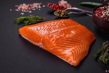 Fillet of raw red salmon fish with salt, spices and herbs on a dark concrete background