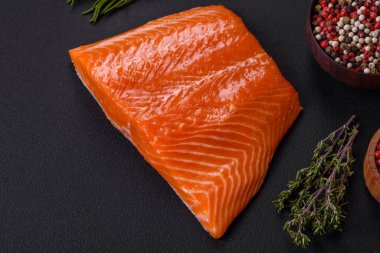 Fillet of raw red salmon fish with salt, spices and herbs on a dark concrete background