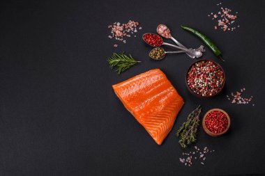Fillet of raw red salmon fish with salt, spices and herbs on a dark concrete background