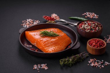 Fillet of raw red salmon fish with salt, spices and herbs on a dark concrete background