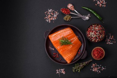 Fillet of raw red salmon fish with salt, spices and herbs on a dark concrete background