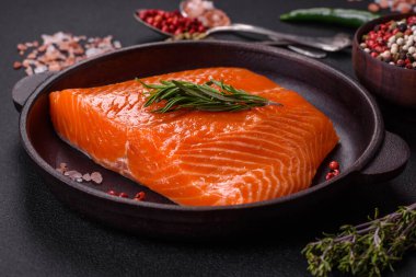 Fillet of raw red salmon fish with salt, spices and herbs on a dark concrete background