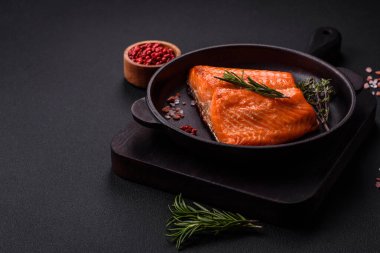 Delicious baked salmon red fish steak with spices and herbs on a dark concrete background